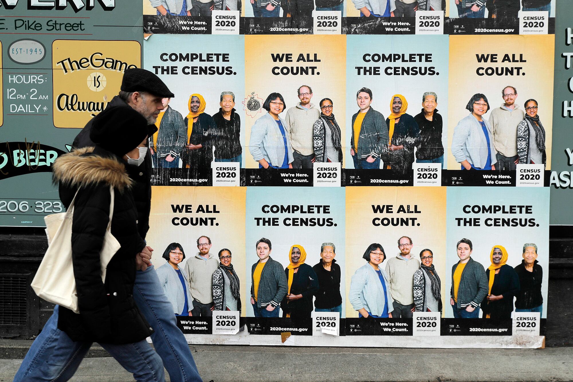 In this April 1, 2020, file photo, people walk past posters encouraging participation in the 2020 Census in Seattle's Capitol Hill neighborhood.